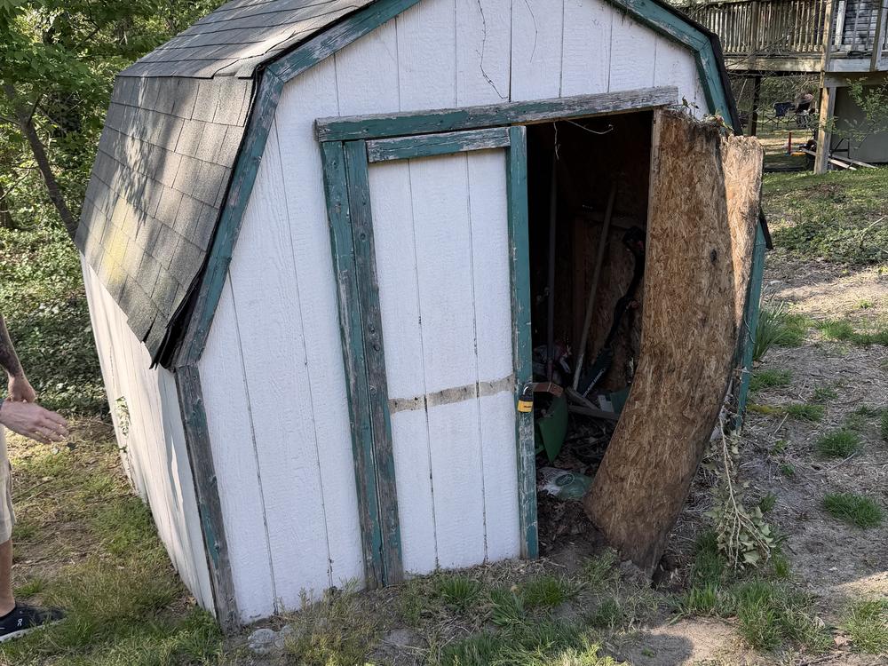 Old barn-roof storage shed with a sagging roof and open door before demolition on Mountain View Circle in Glen Burnie, MD