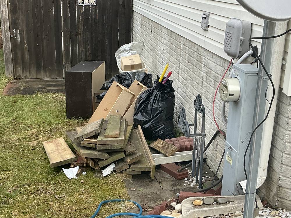 Scrap wood, bagged trash and old fencing piled along the side of a house before removal in Walnut Grove, Glen Burnie, MD
