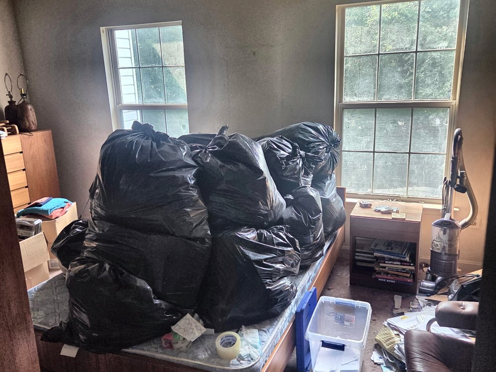 Bedroom with the bed piled full of stuffed black trash bags before an estate cleanout on Icy Run Terrace in Odenton, MD